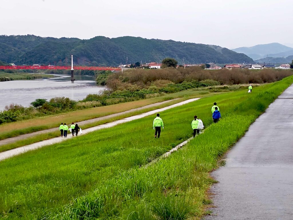 alt="高橋建設社員が益田市の高津川左岸でペットボトルや空き缶を回収する清掃活動の様子"