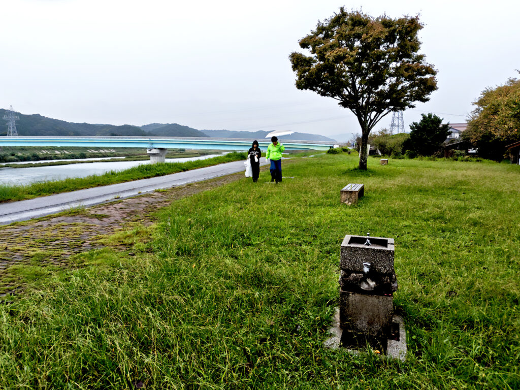 alt="高橋建設社員が益田市の高津川左岸でペットボトルや空き缶を回収する清掃活動の様子"